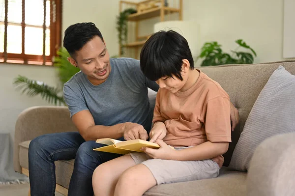 친절하고 아시아인 아버지는 아들에게 거실에 소파에서 읽거나 가르치고 있습니다 홀어머니의 — 스톡 사진