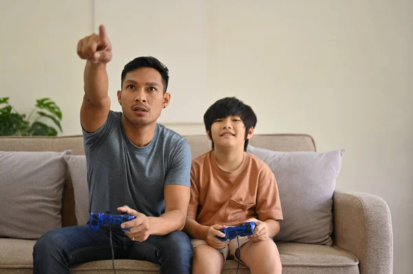 Joyful and excited Asian dad and son with joysticks are playing video games together at home. entertainment and family concept