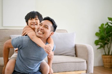 Neşeli ve mutlu Asyalı baba, küçük oğluyla oturma odasında oynuyor, sırtında taşıyordu, uçakla oynuyordu, evde birlikte eğleniyordu..