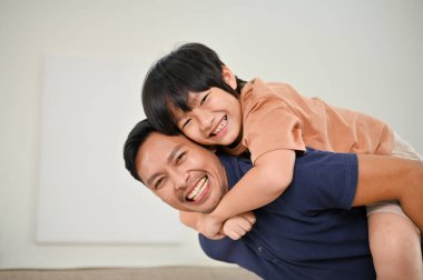 Mutlu Asyalı oğul ve baba evde birlikte eğleniyor, oturma odasında oynuyorlar ve sırtımda taşıyorlar. Mutlu aile ve bekar baba kavramı