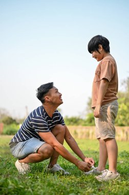 Önemseyen Asyalı bir baba arka bahçede oğlu için ayakkabı bağcıkları bağlıyor. açık hava aktivitesi ve aile kavramı