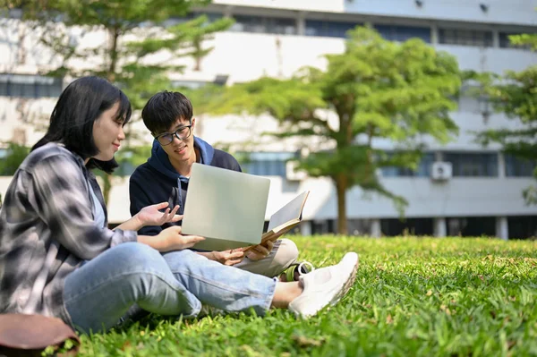 两个快乐聪明的年轻亚洲大学生坐在校园公园的草地上 一边分享他们的想法 一边聊天 一边做功课 — 图库照片