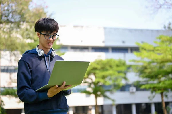 在大学公园里 聪明而快乐的年轻亚洲大学生正在使用他的手提电脑 — 图库照片