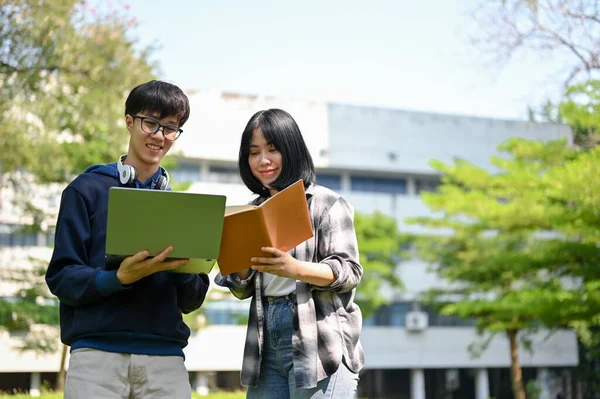 快乐的亚洲男女大学生站在校园前 手里拿着笔记本电脑和课本 — 图库照片