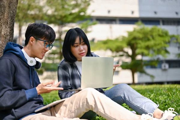 两名聪明而快乐的亚洲大学生正在校园公园里讨论 一边看电脑屏幕 一边一起学习功课 — 图库照片