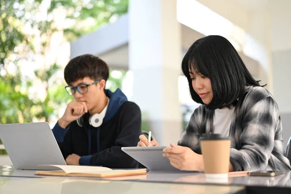 漂亮聪明的年轻亚洲女大学生在平板电脑上做功课 而她的男朋友则在笔记本电脑上做作业 坐在校园里 — 图库照片