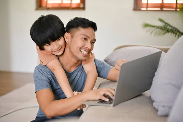 귀여운 아시아인 거실에서 노트북으로 일하는 뒤에서 아버지를 껴안고 있습니다 아시아인 — 스톡 사진