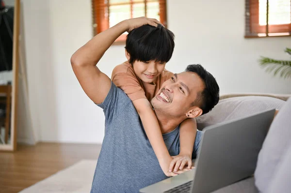 귀여운 아시아인 거실에서 노트북으로 일하는 뒤에서 아버지를 껴안고 — 스톡 사진