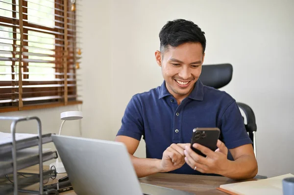 一个微笑成功的千年亚洲商人在他的工作空间用他的手机 技术和人的概念 — 图库照片