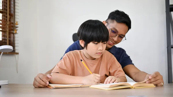 Søt Asiatisk Gutt Som Fokuserer Lekser Mens Faren Underviser Hjelper – stockfoto