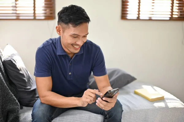 千年快乐的亚洲男人在客厅里放松的同时 还在社交媒体上和朋友聊天 — 图库照片