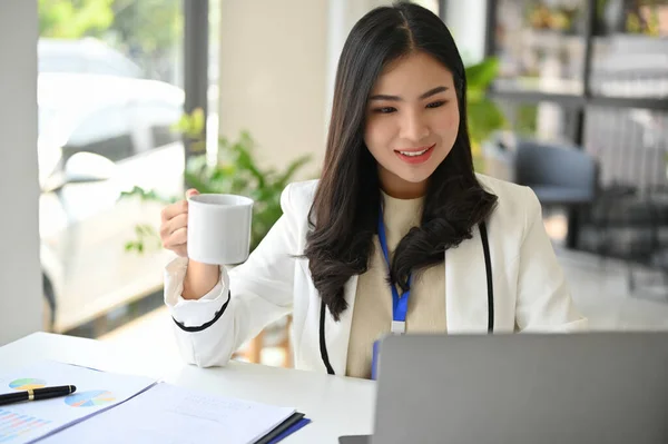 优雅而专业的千年亚洲女商人或女经理在办公室边喝咖啡边用笔记本电脑做新项目 — 图库照片