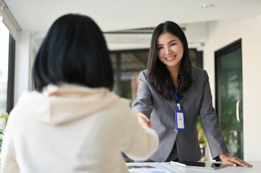 Çekici ve çekici Asyalı iş kadını ya da kadın bankacı ofiste müşterisiyle el sıkışıyor..