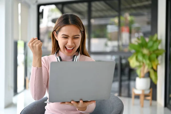 Excited and cheerful millennial Asian woman looking at her laptop screen, rejoicing, and screaming with joy. good news, lottery winning, getting job promotion