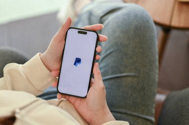 Chiang Mai, Tayland - 31 Mart 2023: Akıllı telefonunda PayPal kullanan bir kadın. Ekranda PayPal logosu olan iPhone. yakın plan resim