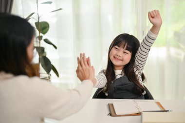 Asyalı bir anne, sevimli küçük kızına beşlik çakarken evde birlikte güzel vakit geçiriyor. eğlence ve eğitim kavramı