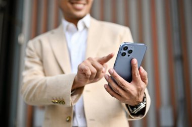 Bin yıllık yakışıklı Asyalı işadamı ya da takım elbiseli erkek CEO bir şehirde dururken akıllı telefonunu kullanıyor. metin, sohbet, mesaj, bağlantı