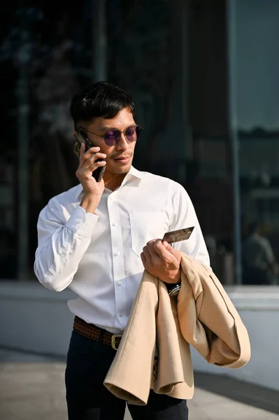 英俊的千年亚洲商人在一个城市散步时 正在用他的信用卡呼叫中心服务打电话 — 图库照片