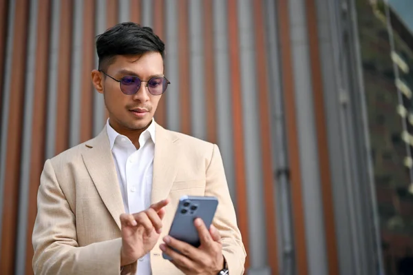 英俊的千年亚洲商人或穿着西装 站在城市时使用智能手机的首席执行官 — 图库照片