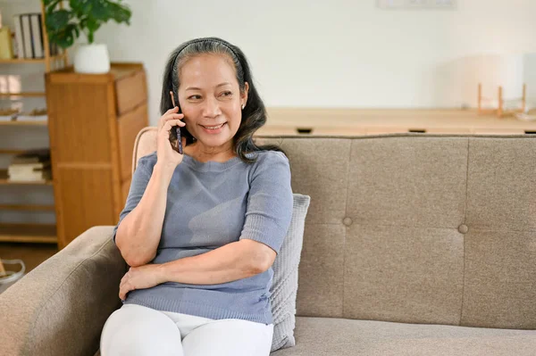 Šťastná Asiatka Důchodu Někým Telefonuje Zatímco Odpočívá Gauči Svém Obýváku — Stock fotografie