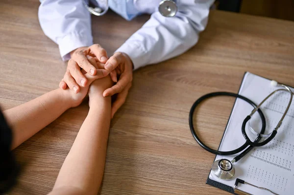Tıbbi konsültasyon sırasında hastayı rahatlatmak ve rahatlatmak için elini tutan bir doktorun yakın çekim görüntüsü. Sağlık ve tıbbi konsept