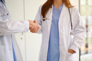 Profesyonel bir kadın doktor hastane koridorunda konuşurken iş arkadaşlarıyla tokalaşıyor. kırpılmış resim