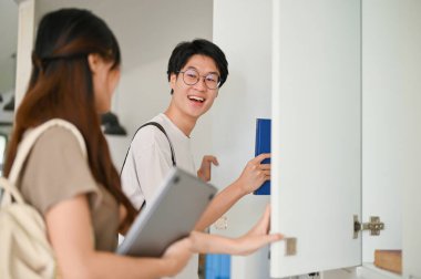 Neşeli ve mutlu Asyalı bir üniversite öğrencisi okul koridorunda arkadaşıyla konuşuyor..
