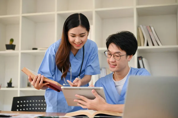 Two smart young Asian medical students are talking, using tablet and researching medical online papers together.