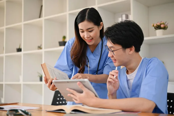 两名身穿制服的聪明专注的年轻亚洲医科学生正在一个图书馆里共同讨论和研究医学信息 — 图库照片