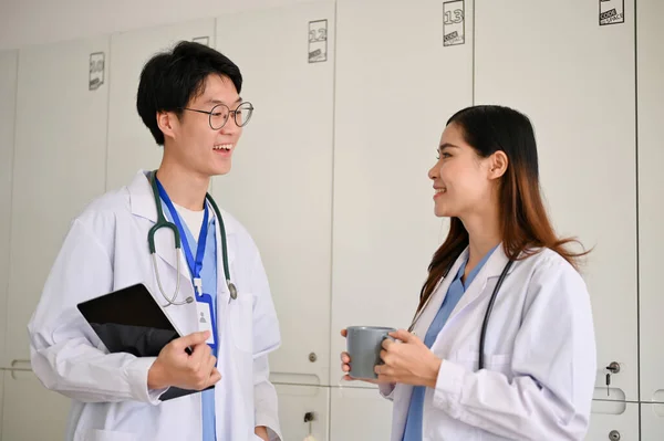 两名年轻的亚洲医科学生在医院的走廊边喝咖啡边聊天 他们快乐而轻松 — 图库照片