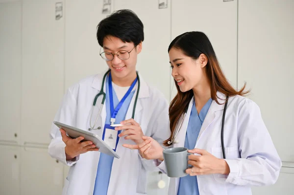 聪明的年轻亚洲男性医生或医科学生在喝咖啡时间和一位女同事一起讨论他的医疗案例 一起看平板电脑屏幕 — 图库照片
