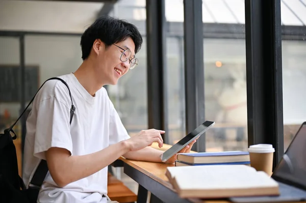 聪明英俊的年轻亚洲大学生 用他的数码平板电脑 在一家咖啡馆里为学校的项目工作 — 图库照片