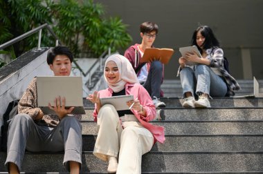 Çekici, genç, Asyalı, Müslüman, okul projesinde erkek arkadaşıyla birlikte kampüs binasının dışındaki merdivenlerde çalışan kız öğrenci. Üniforma yaşam tarzı ve arkadaşlık kavramı