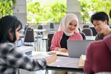 Genç ve güzel bir Asyalı Müslüman üniversite öğrencisi kampüs kafeteryasında arkadaşlarıyla okul grubu projesi yapıyor..