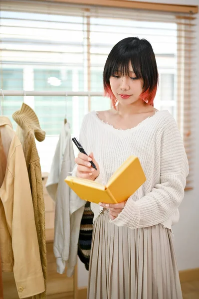 Portrait, Attractive young Asian female fashion clothes shop owner checking her product stock and working in her store. SME business concept