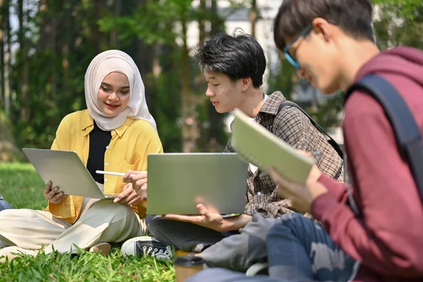 有吸引力的 友善的年轻的亚洲穆斯林女大学生和她的男性朋友在校园公园的草地上和她们的小组一起聊天和讨论工作 — 图库照片