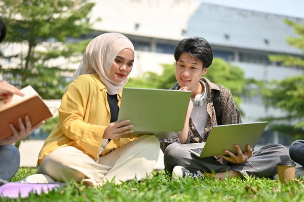 以年轻的亚洲穆斯林女大学生为重点 与她的男性朋友讨论工作 同时在校园公园放松一下 — 图库照片