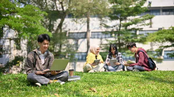 身穿法兰绒衬衫的英俊而快乐的年轻亚洲大学生坐在校园公园的草地上 用他的手提电脑 单一生活方式概念 — 图库照片