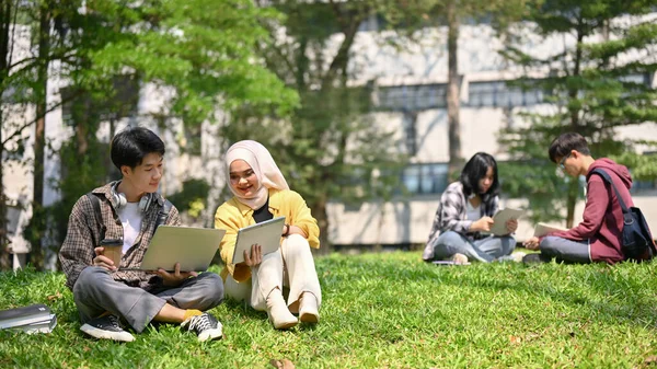 两个快乐的年轻亚洲大学生坐在草地上 一起在校园公园里放松 一边聊天一边做功课 多样性和友谊概念 — 图库照片