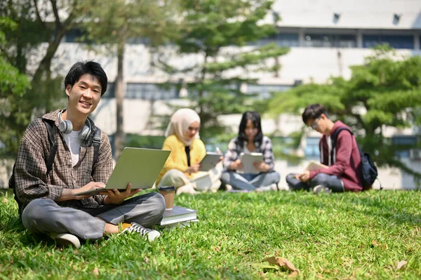 身穿法兰绒衬衫 面带微笑而快乐的年轻亚洲大学生 拿着手提电脑坐在校园公园的草地上 — 图库照片