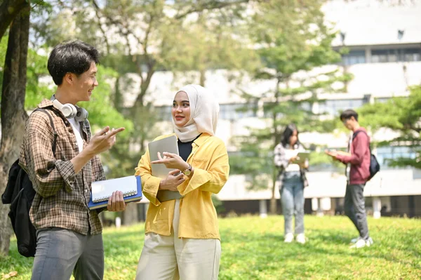キャンパスパークで彼のイスラム教徒の女性の友人と話して幸せと魅力的な若いアジアの男性大学生 — ストック写真