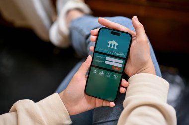 Chiang Mai, Tayland - Nisan 05 2023: Bir kafede dinlenirken cep telefonu uygulamasını kullanan günlük giysiler içindeki bir kadının yakın plan görüntüsü. Ekranda mobil bankacılık logosu olan iPhone.