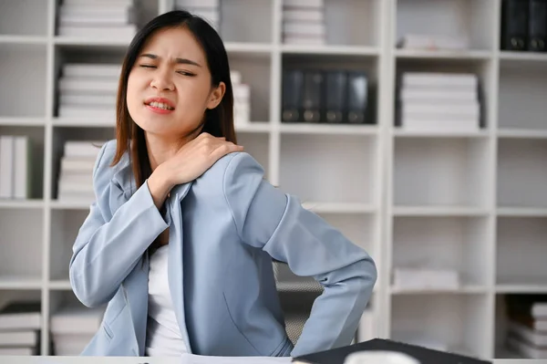 stock image Unwell millennial Asian businesswoman or female office worker suffering from shoulder pain while working in the office. office syndrome concept