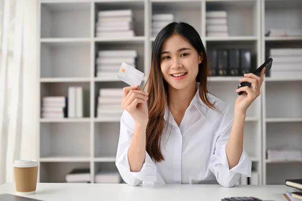 迷人的千年亚洲女性办公室职员坐在办公桌前 手里拿着信用卡和智能手机 移动银行 电子钱包 网上支付 — 图库照片
