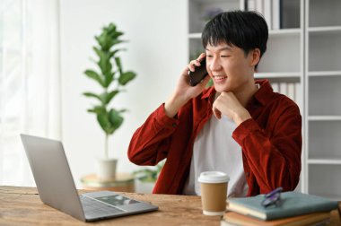 Sevgili Asyalı genç adam çalışma masasında otururken arkadaşıyla telefon görüşmesi yapıyor.. 