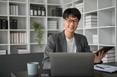 Ofis odasında çalışan zeki genç bir iş adamı. Ofis masasında oturan beyaz dizüstü bilgisayar.. 