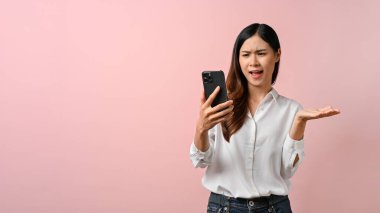 Akıllı telefona kafa karıştırıcı düşüncelerle bakan genç bir kadın resmi, pembe arka planda gömlekli.. 