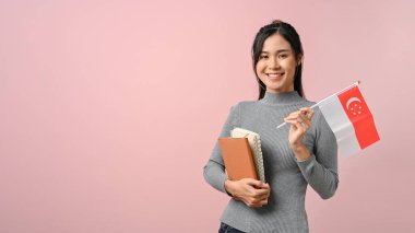 Güzel Asyalı öğrenci Singapur bayrağını pembe yalıtılmış arka planda, eğitim konseptinde gösteriyor. Yurtdışında eğitim.