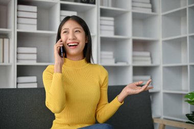 Genç ve çekici Asyalı bir kadın evdeki kanepede otururken arkadaşlarıyla telefon görüşmesi yapıyor..