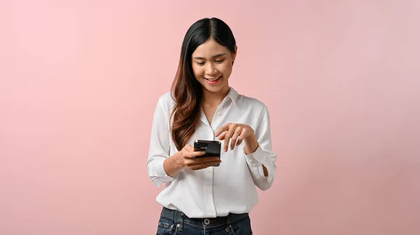 快乐的年轻亚洲女人在智能手机上用粉色背景隔离留言 — 图库照片